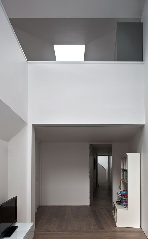 White high ceilings and walls with wooden floors. on the left is a low white cabinet with a black flat screen tv on it, while on the right is a white L shaped cabinet