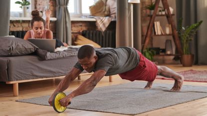 Man using an ab roller at home on a wooden floor