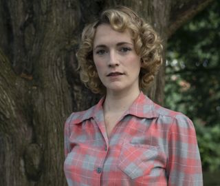 Bonnie (Charlotte Ritchie) stands in front of a tree wearing a pink and blue plaid flannel shirt