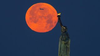 the full moon can be seen behind the statue of liberty