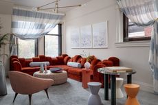 A family room with a large, red couch, a gray carpet and three small stools in varied colors 