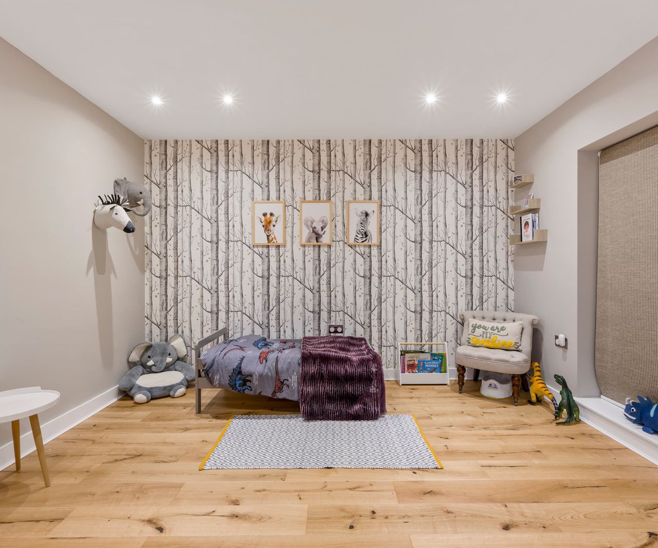 A children's bedroom with tree wallpaper and animal designs and toys