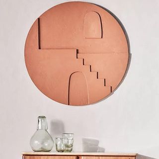 A terracotta textured piece of wall art in a circular shape