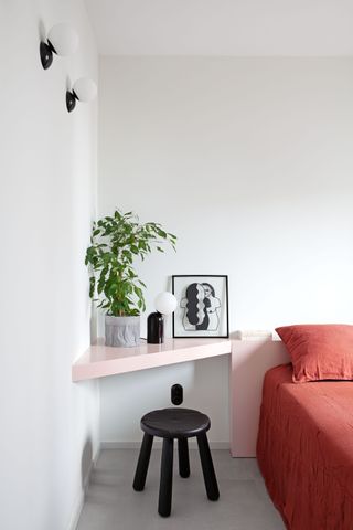 A bedroom with white walls, pastel pink shelves and dark pink bedding