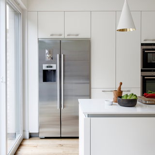 Kitchen with white cabinets, wall, lamps, and kitchen peninsula, wooden floor, metal fridge, and colourful decorative touches.