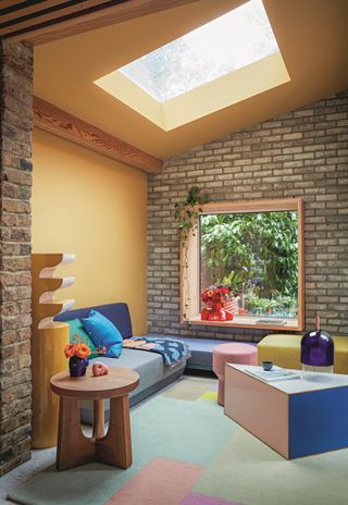 A living room with bold shapes and colours, an exposed brickwork wall and colourful blocked carpet, and blue and green colours, under a skylight