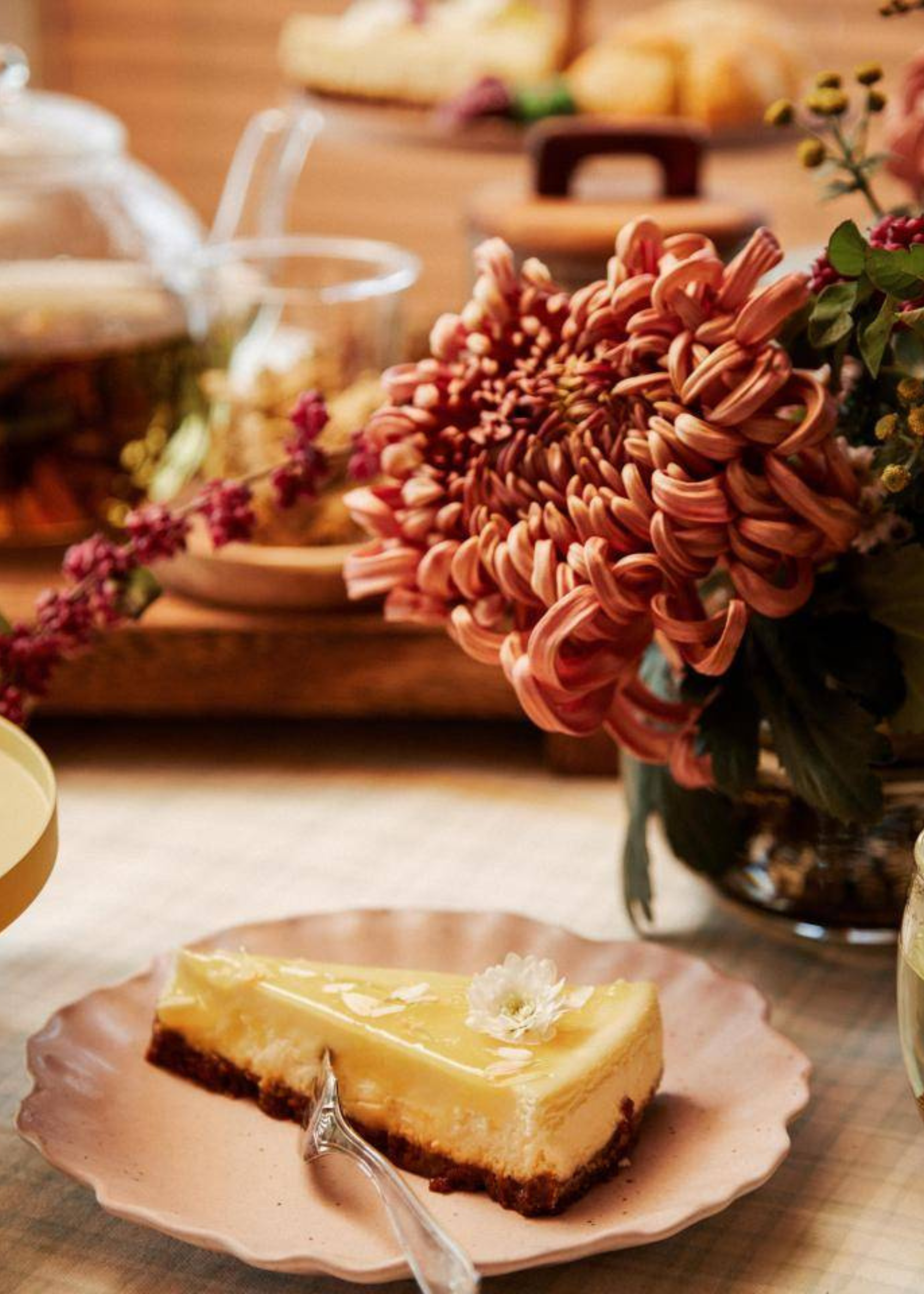 A close-up of a chrysanthemum in a vase by a plate of cheesecake