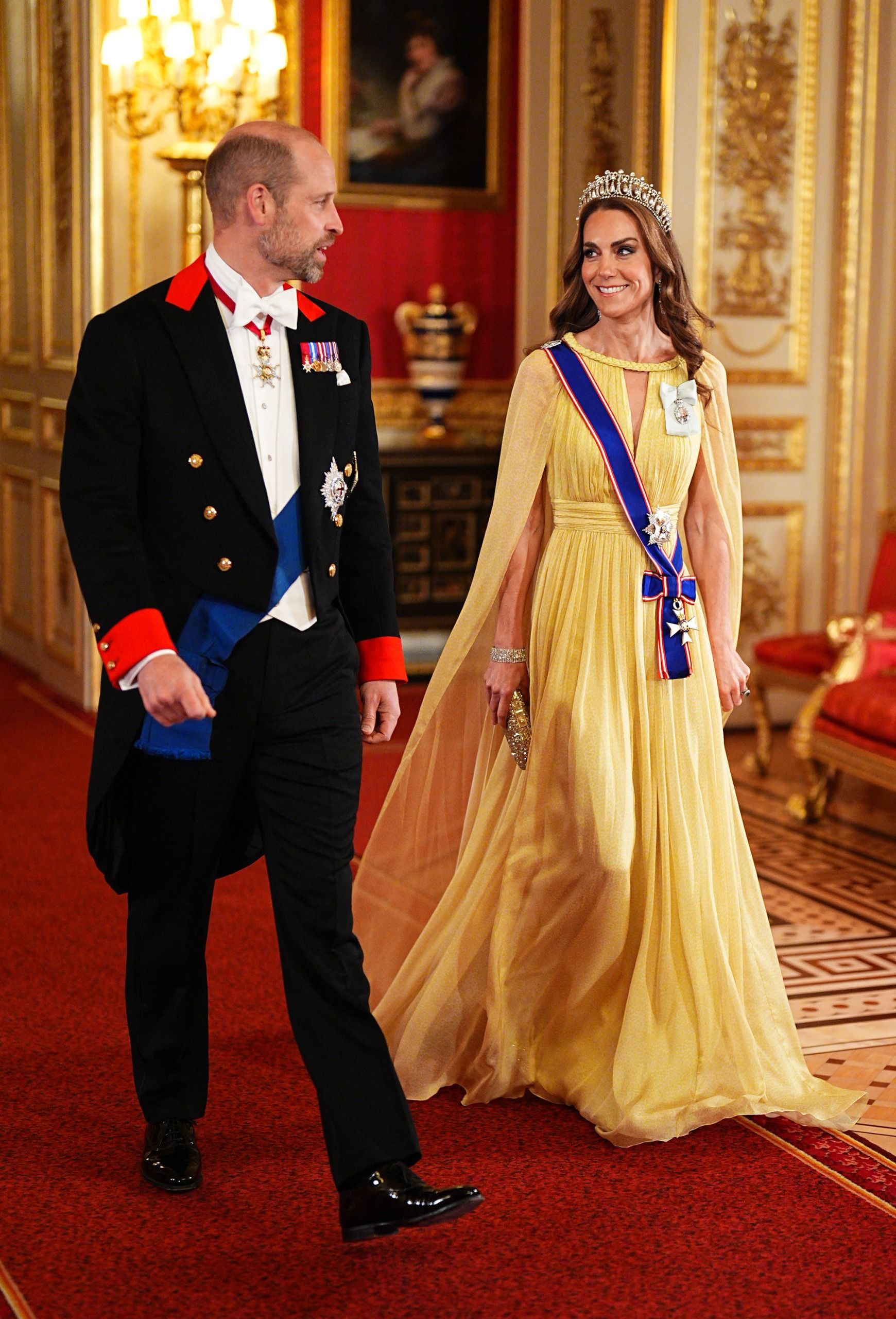 Princess Kate wearing a tiara and yellow gown walking with Prince William at the Omani state banquet