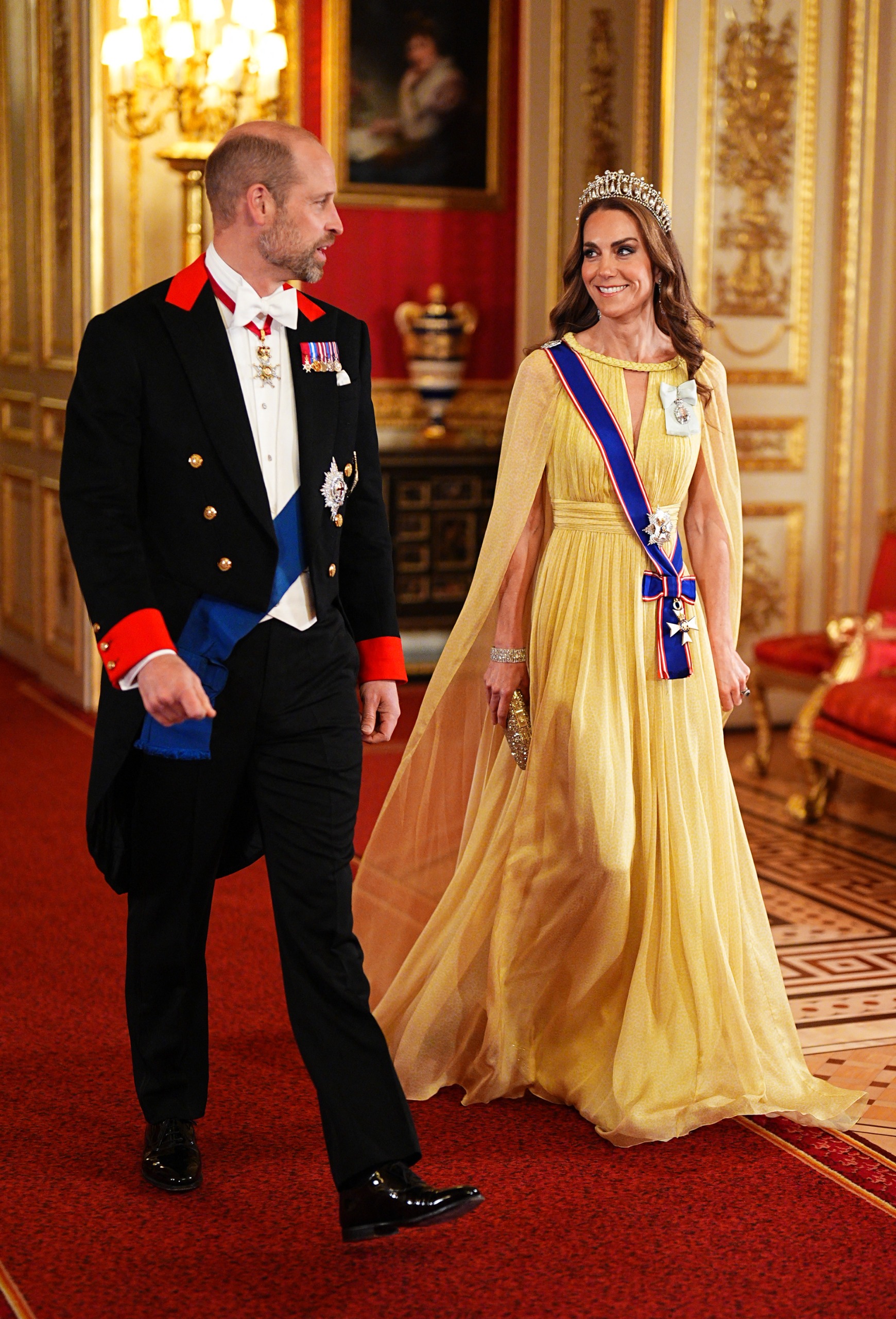 Princess Kate wearing a tiara and yellow gown walking with Prince William at the Omani state banquet