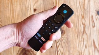 The Amazon Fire TV Stick in a hand above a wooden table.