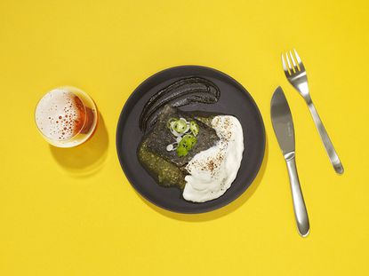 A dish with glass full of beverage and knife and spoon