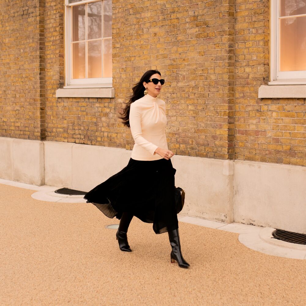 woman walks with long sleeve white top and long black skirt with tall boots