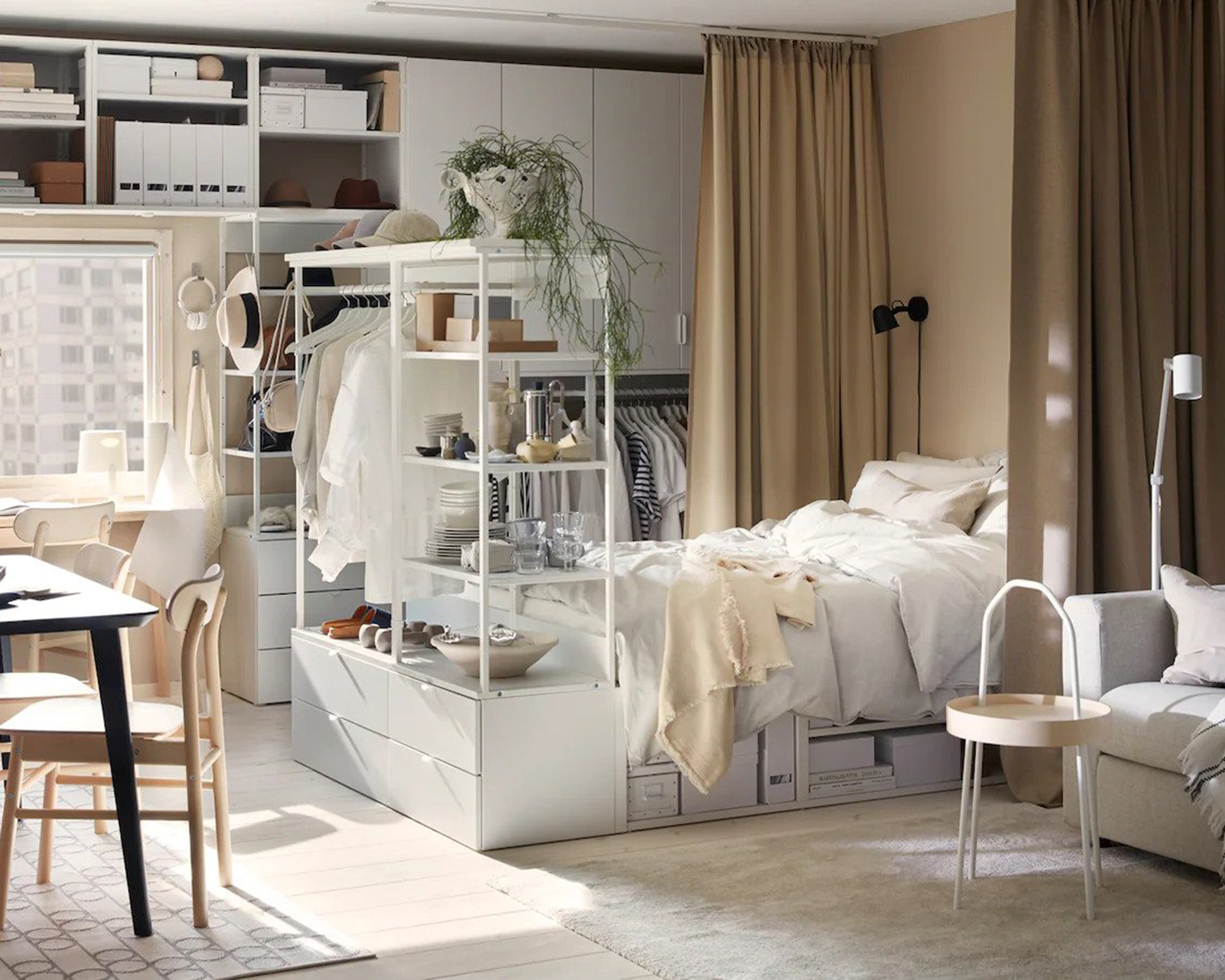 A studio apartment with bed, PLASTA storage unit by Ikea, dining table with chairs and lounge area