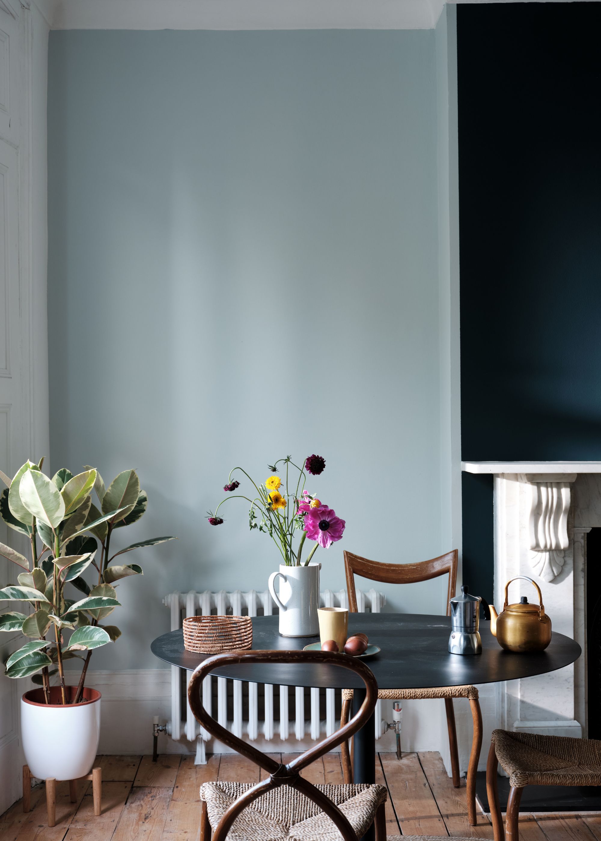 Dining space with pale blue wall, navy blue accent wall, black round dining table with two wooden chairs