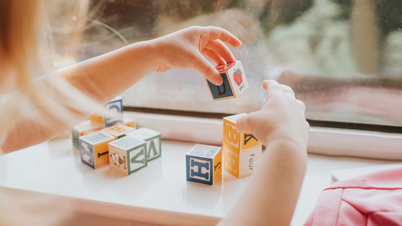 A young girl plays with blocks on a windowsill.