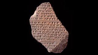 A broken clay tablet with cuneiform against a black background. 