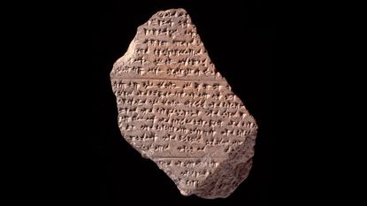 A broken clay tablet with cuneiform against a black background.