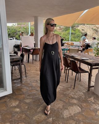 Stilvolle Frau im schwarzen Kleid und Flip-Flops im Urlaub