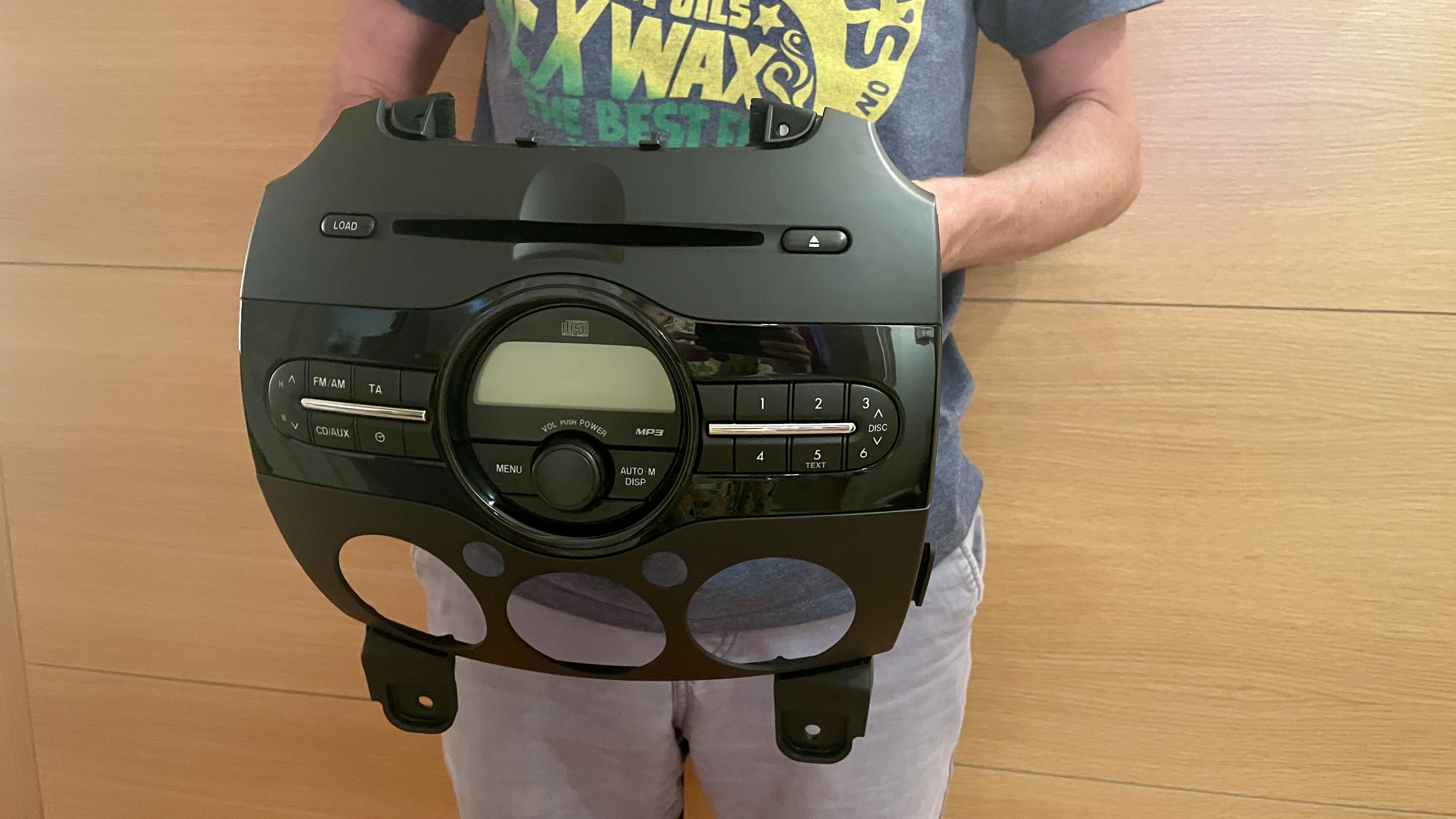 A man holding the central dash column (with Sony CD player) for a Mazda, on wooden background