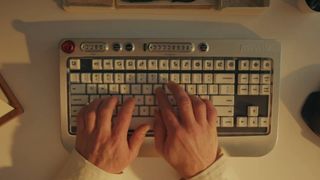 The Freewrite Wordrunner is seen in operation on a white desk. The wordcounter in the centre and the session timer on the left of the keyboard's top edge are ticking up as hands type upon its surface.