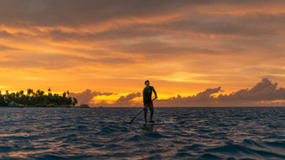 A man paddle boards at sea at sunset