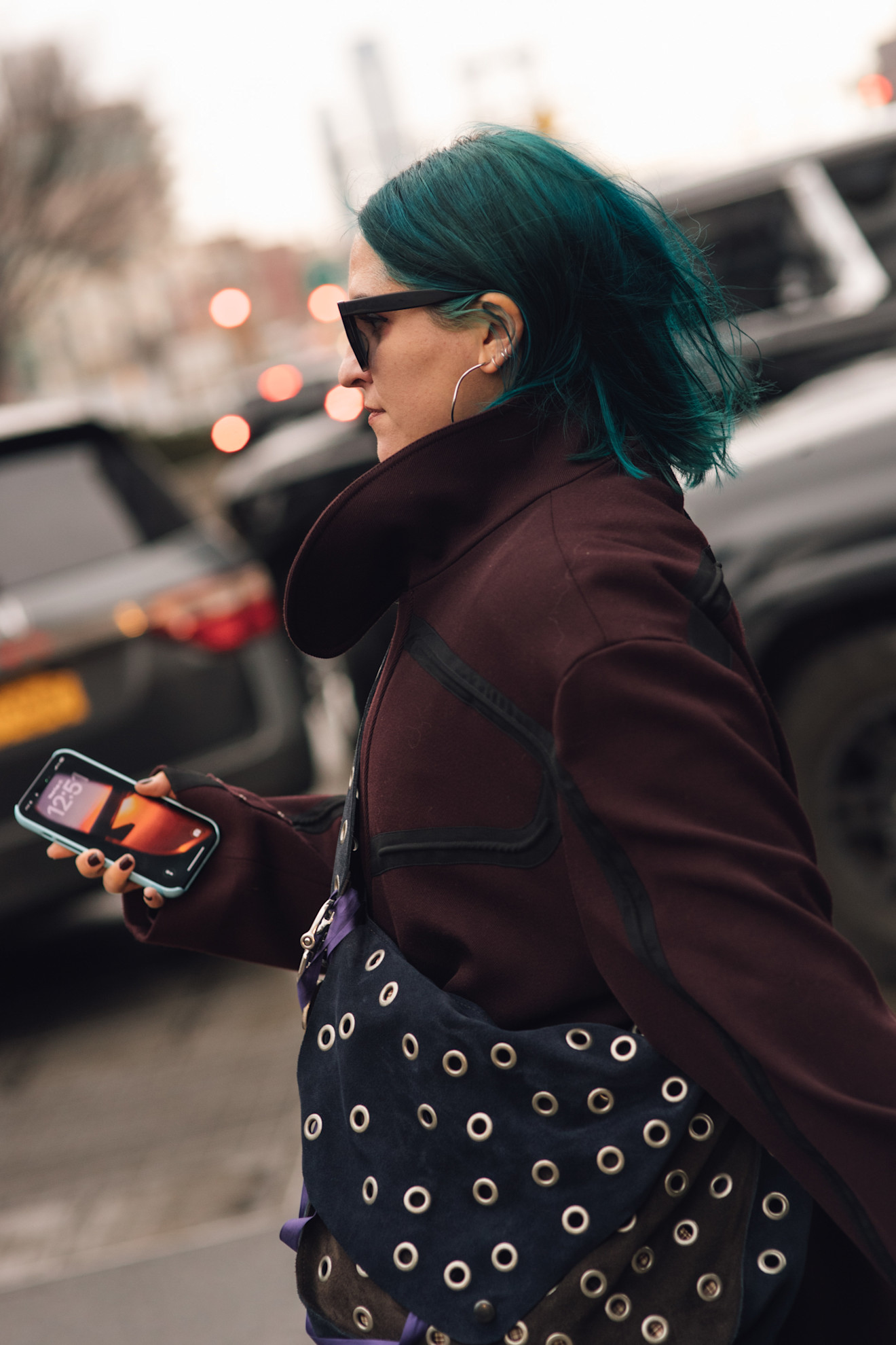 a woman with green hair in a maroon jacket with a black studded bag