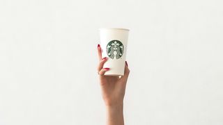 A hand holds a Starbucks coffee cup