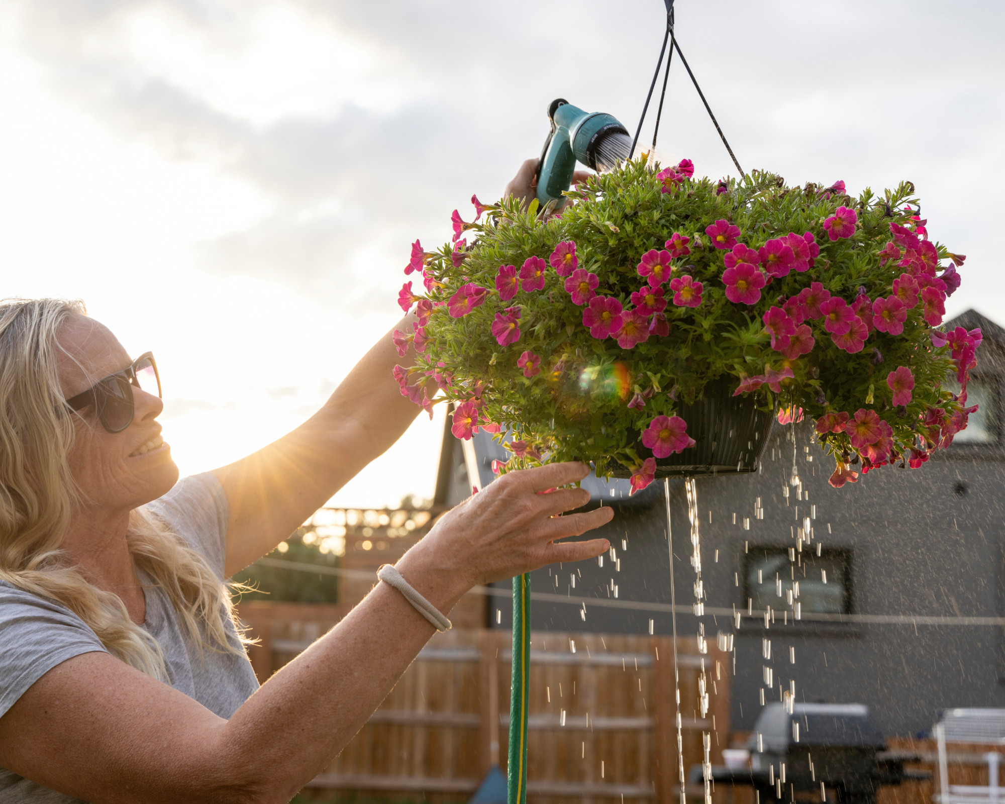 woman watering a hanging basket using a hose pipe, with lots of wasted water dripping from the base