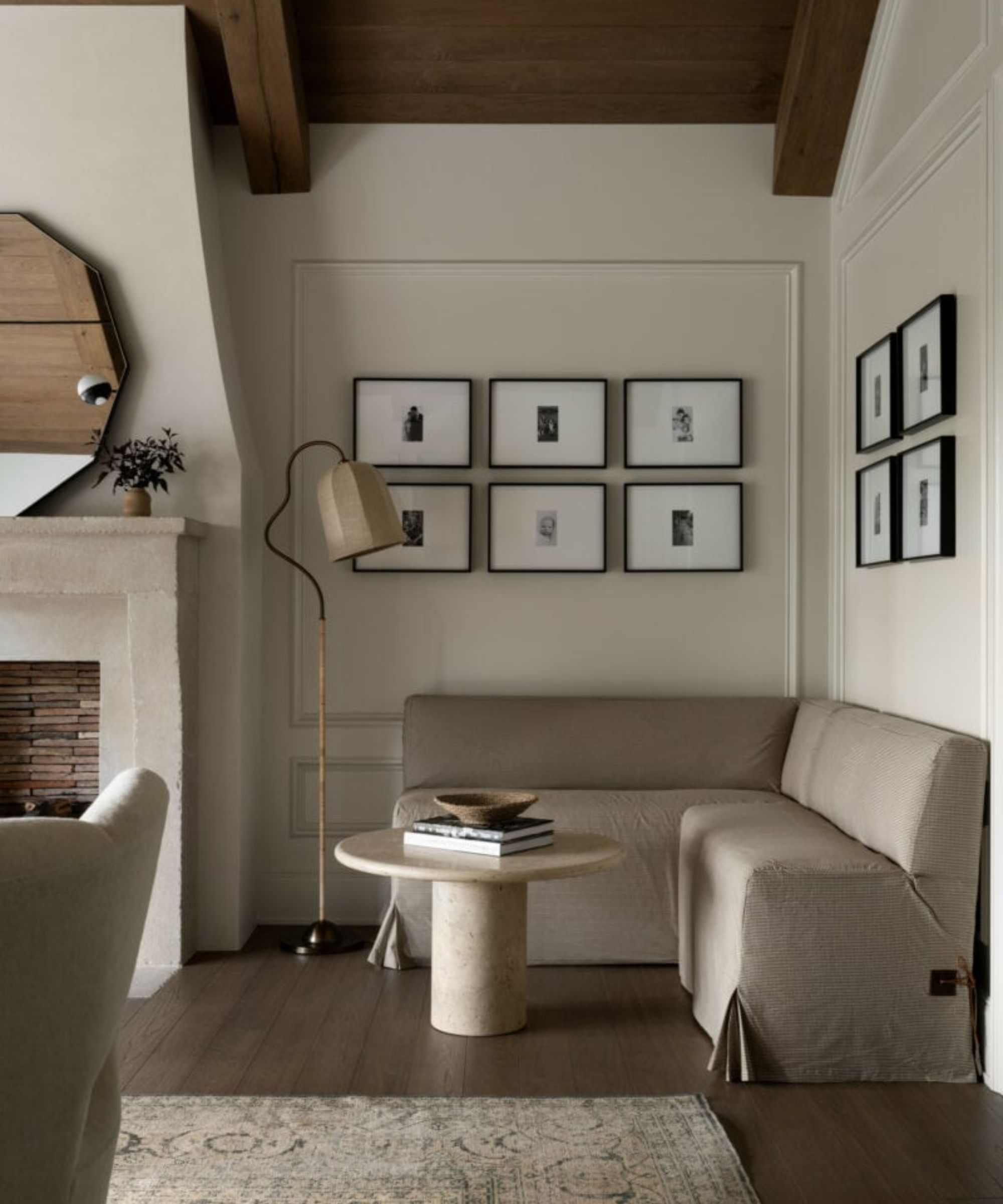 neutral rustic and moody bedroom designed by studio mcgee with a fireplace and a corner banquette seat in neutral linen upholstery styled with a small marble table with a stack of books