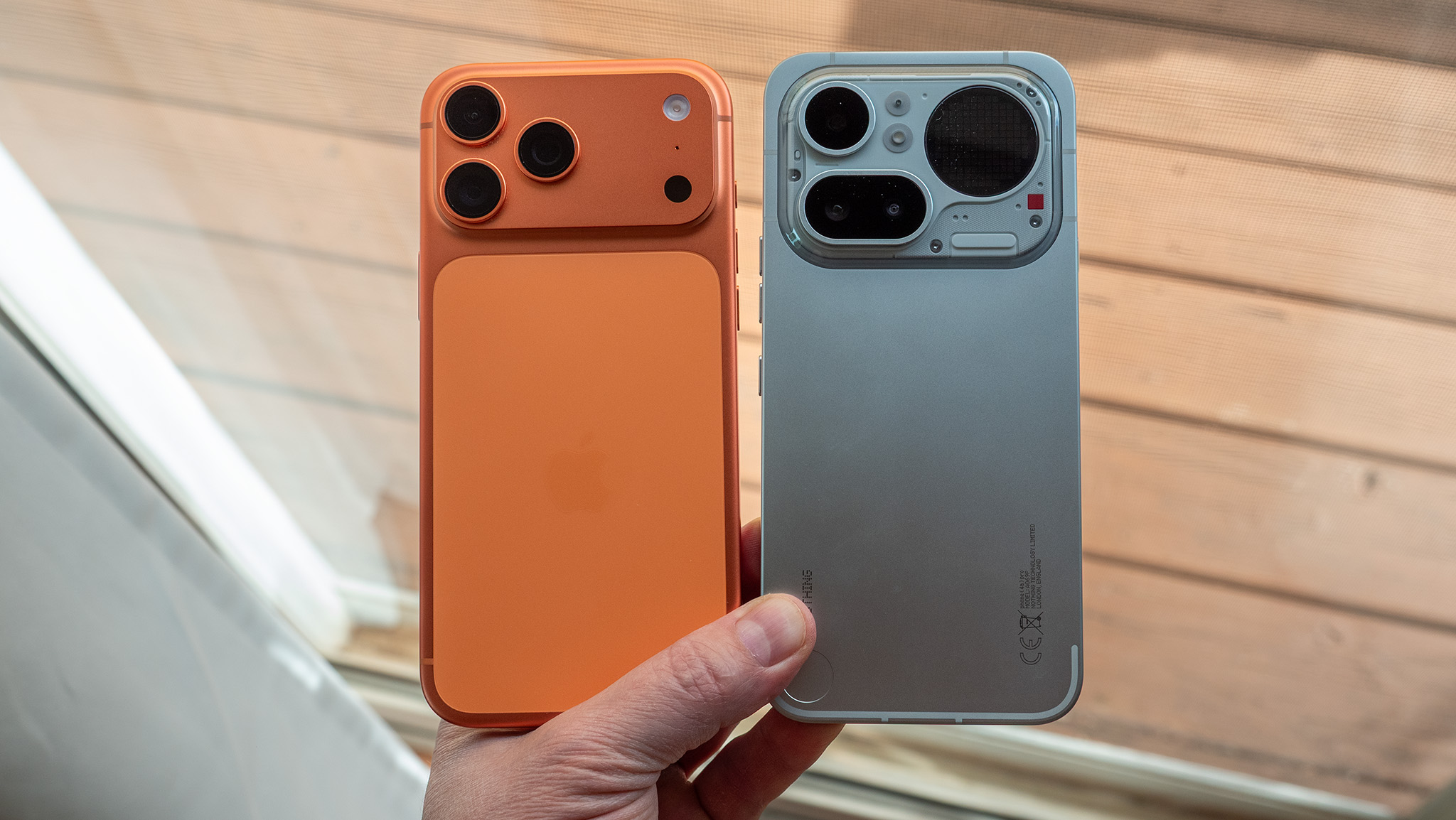 An orange iPhone 17 Pro Max next to a silver Nothing Phone 4a Pro