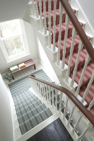 White painted staircase with wooden handrail and runners in same pattern but different colours from Roger Oates