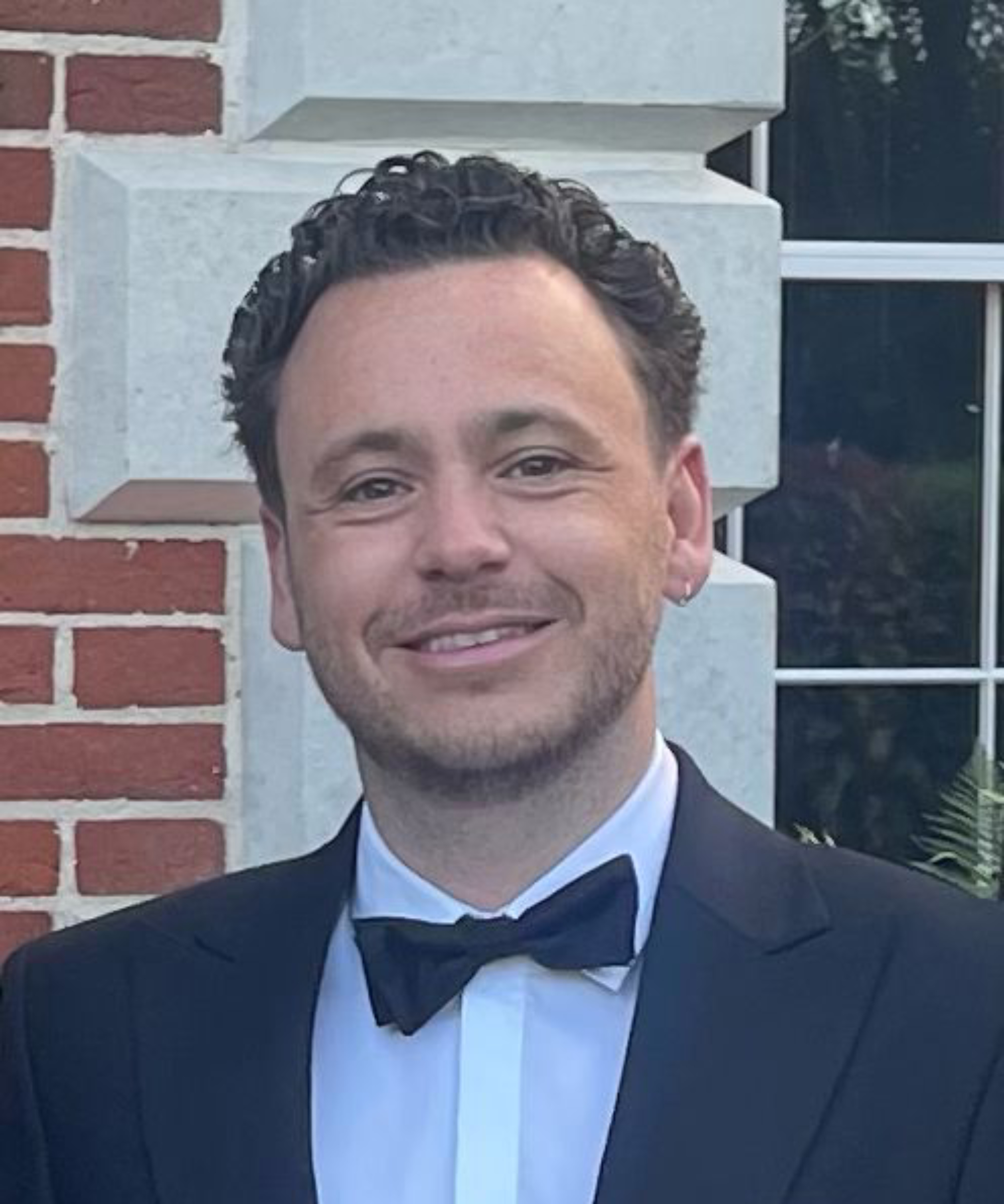 male with dark curly hair wearing dinner jacket, white shirt and bow tie