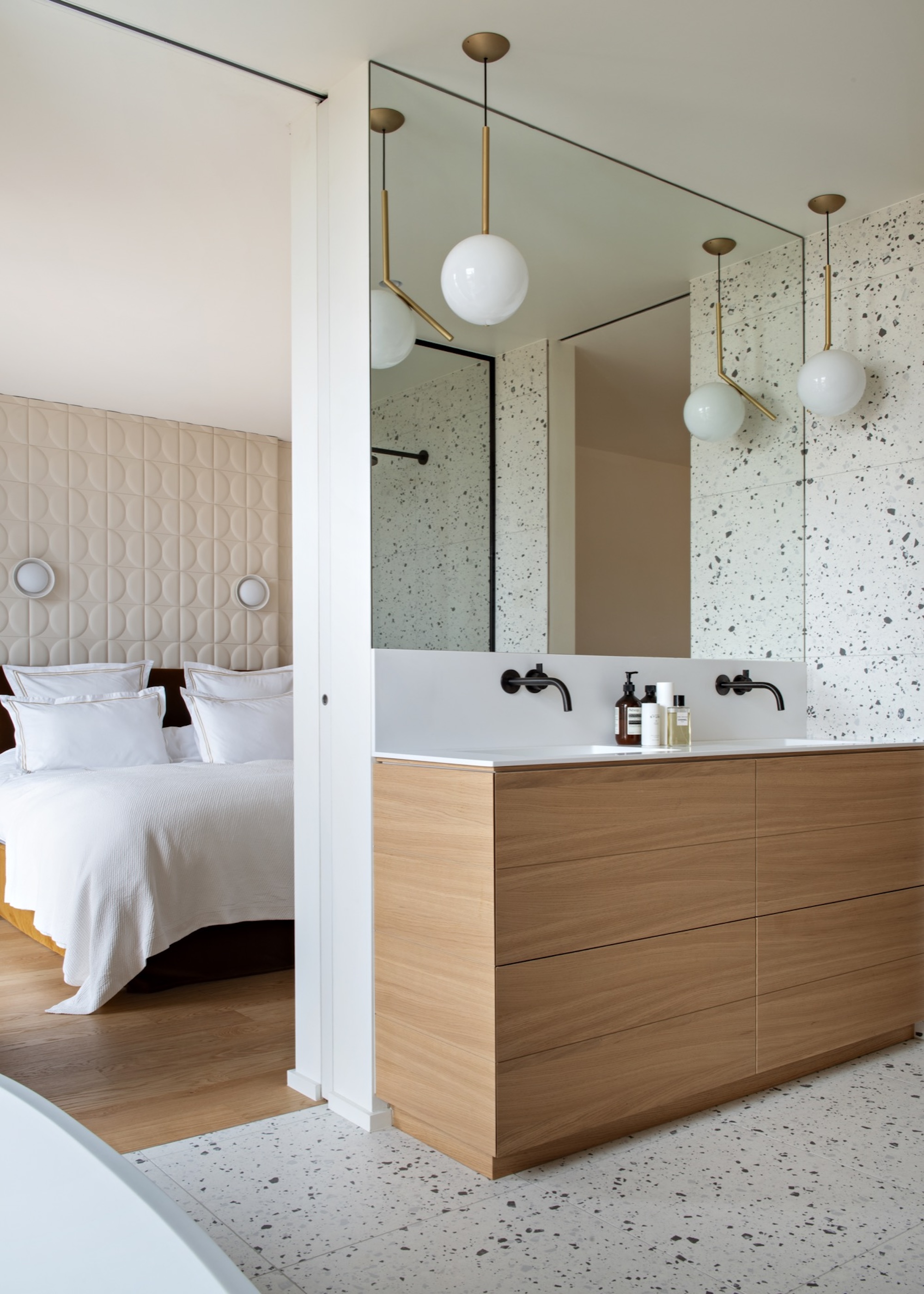 A large mirror in a bathroom above a double sink and a view of a bedroom in the corner
