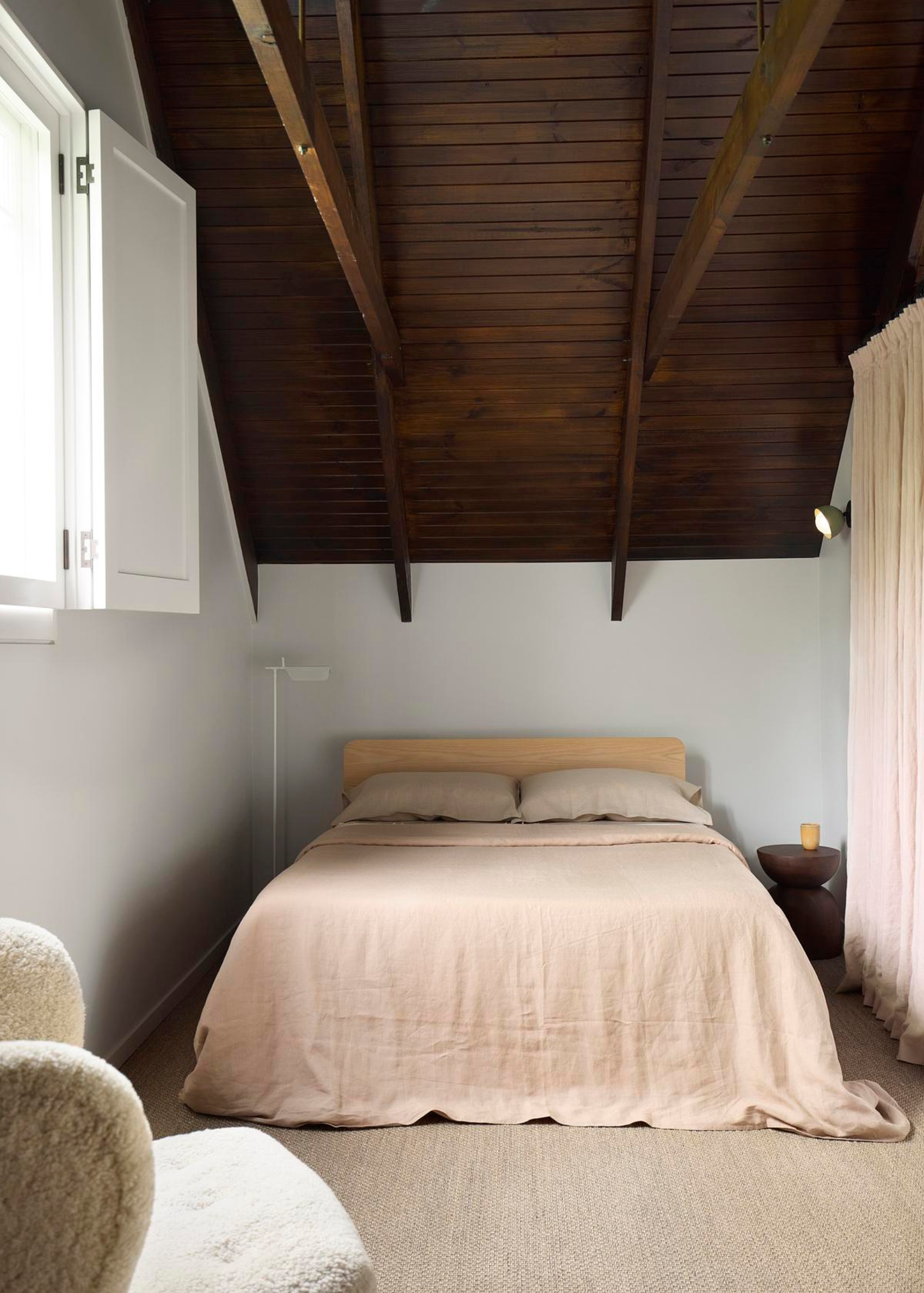 A calm bedroom with vaulted wooden ceilings and a neutral bedscape