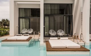 Hotel balcony's with glass sliding doors, white wire frame chairs and loungers extending right to the edge of the pool.