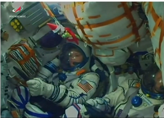 A Christmas elf embraces a dragon stuffed toy (top of picture) during the launch of Expedition 58 on Dec. 3, 2018. The dragon belongs to the son of NASA astronaut Anne McClain, who is pictured just below the floating toys. This picture is a screenshot of a launch video. 