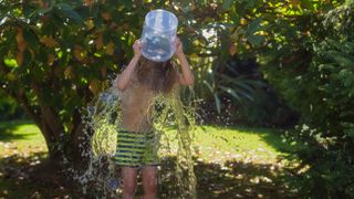 A boy in a swimsuit dumps a bucket of water over his head