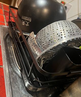 A black dish drying rack stacked with a black pot and silver steamer