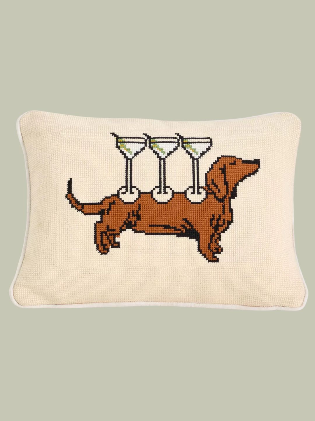 A cotton needlepoint cushion with a dachshund carrying martini glasses