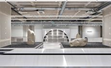 Interior view of a store in Stuttgart designed by Vaust studio featuring light coloured walls and floors, an arched display area, steel stands, display cases filled with black granite and large faux stones made from Styrofoam