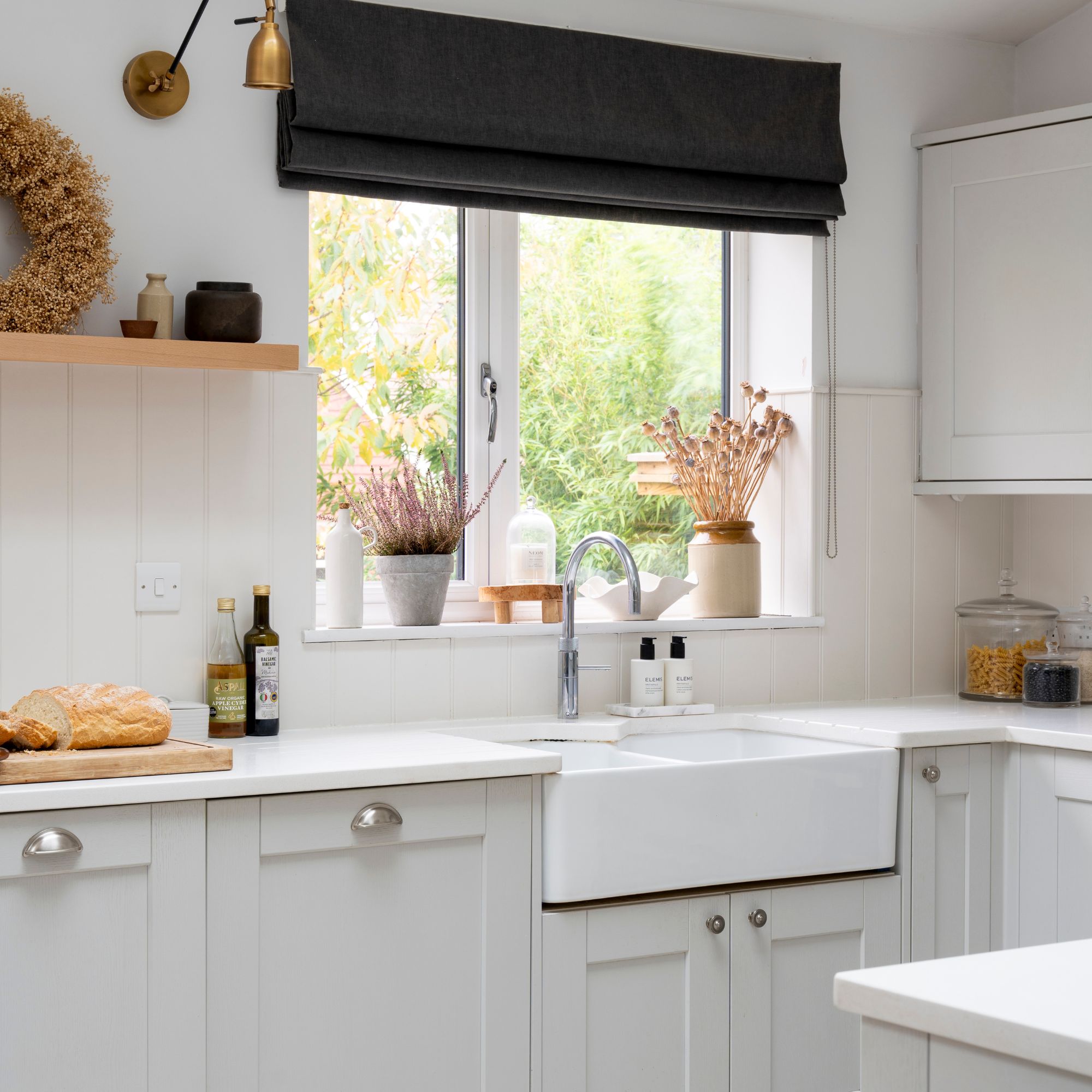 White painted kitchen with a black blind above the window above the sink, with white shaker-style kitchen cabinets