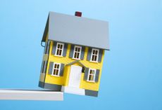 Miniature model of yellow single family house about to fall off edge