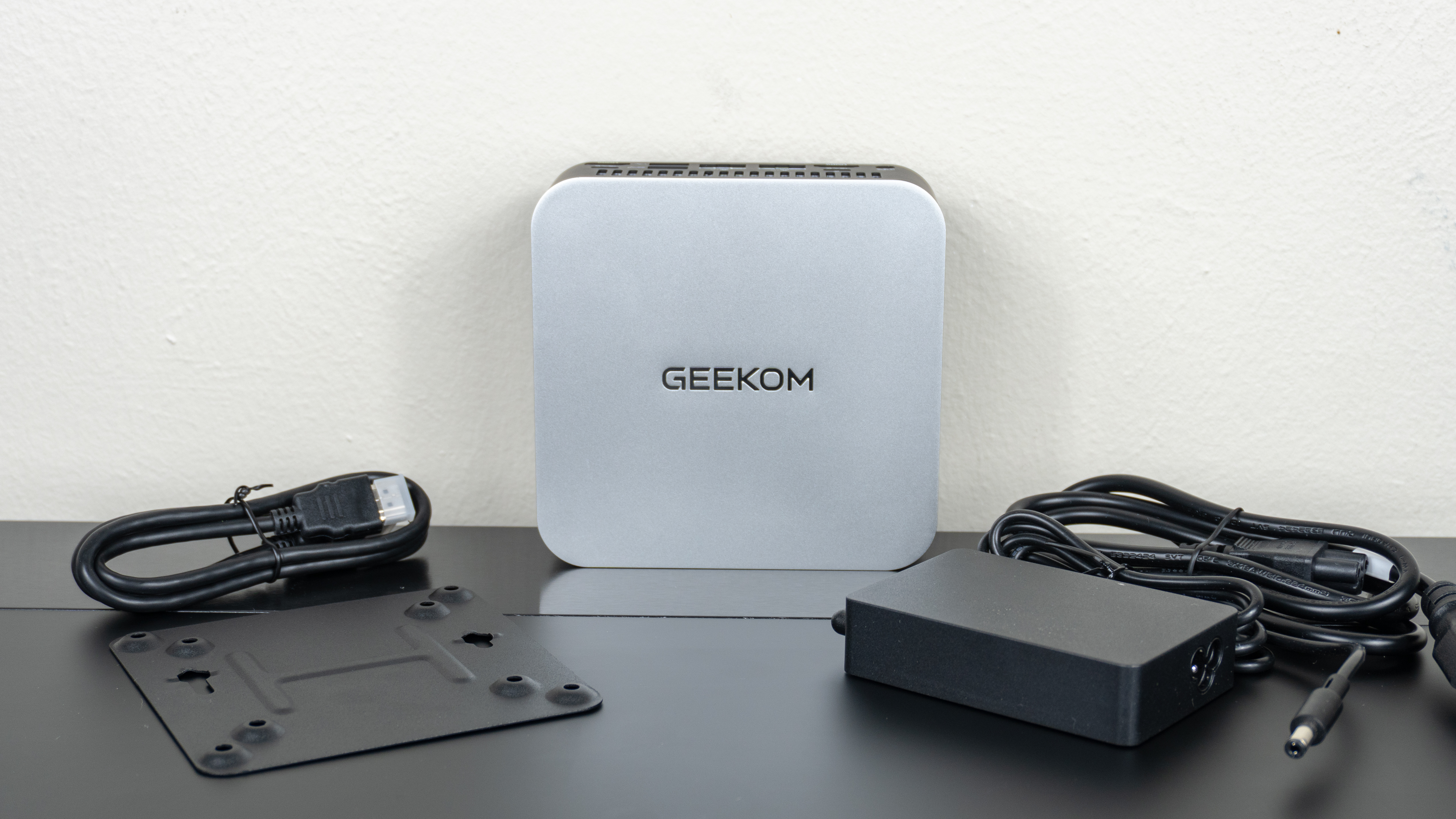The Geekom A9 Max 2026 Edition on a desk with its power adapter and included accessories