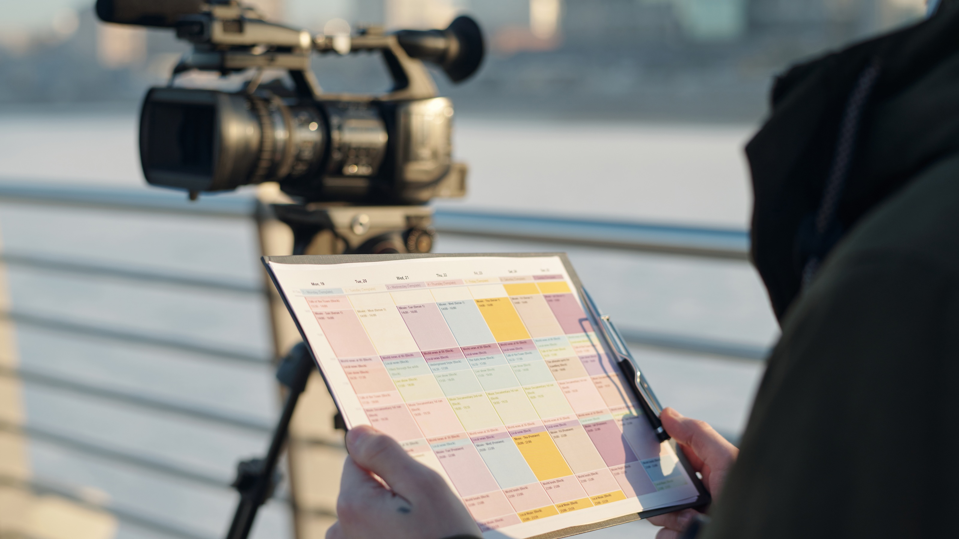 A worker looks at a clipboard while standing near a TV camera.