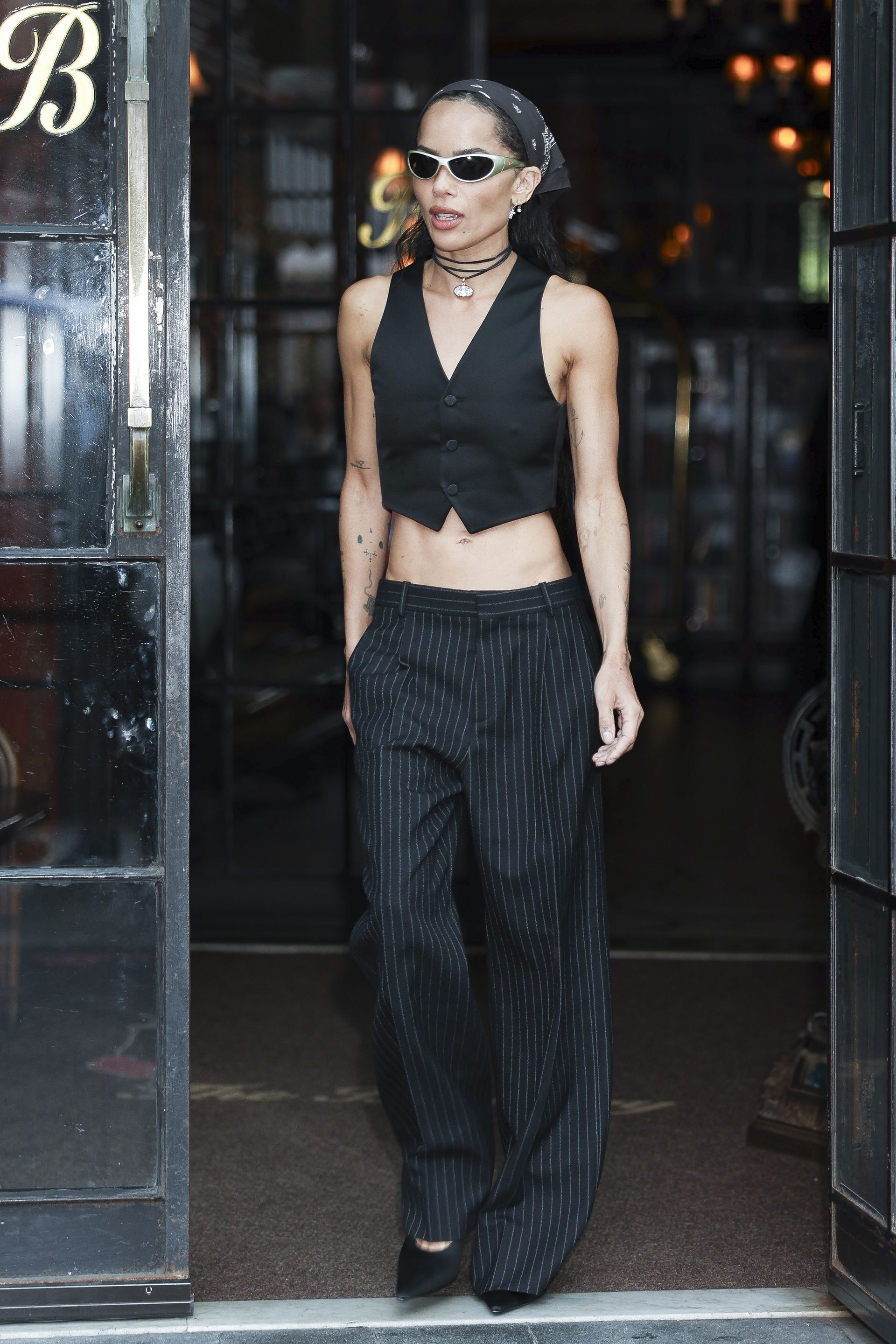 An image of Zoë Kravitz wearing a waistcoat, pinstripe trousers and a bandana as part of her autumn capsule wardrobe.