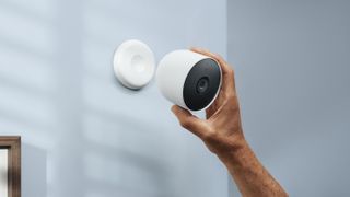 A hand reaching up to place the Nest Cam on its wall mount on an internal wall