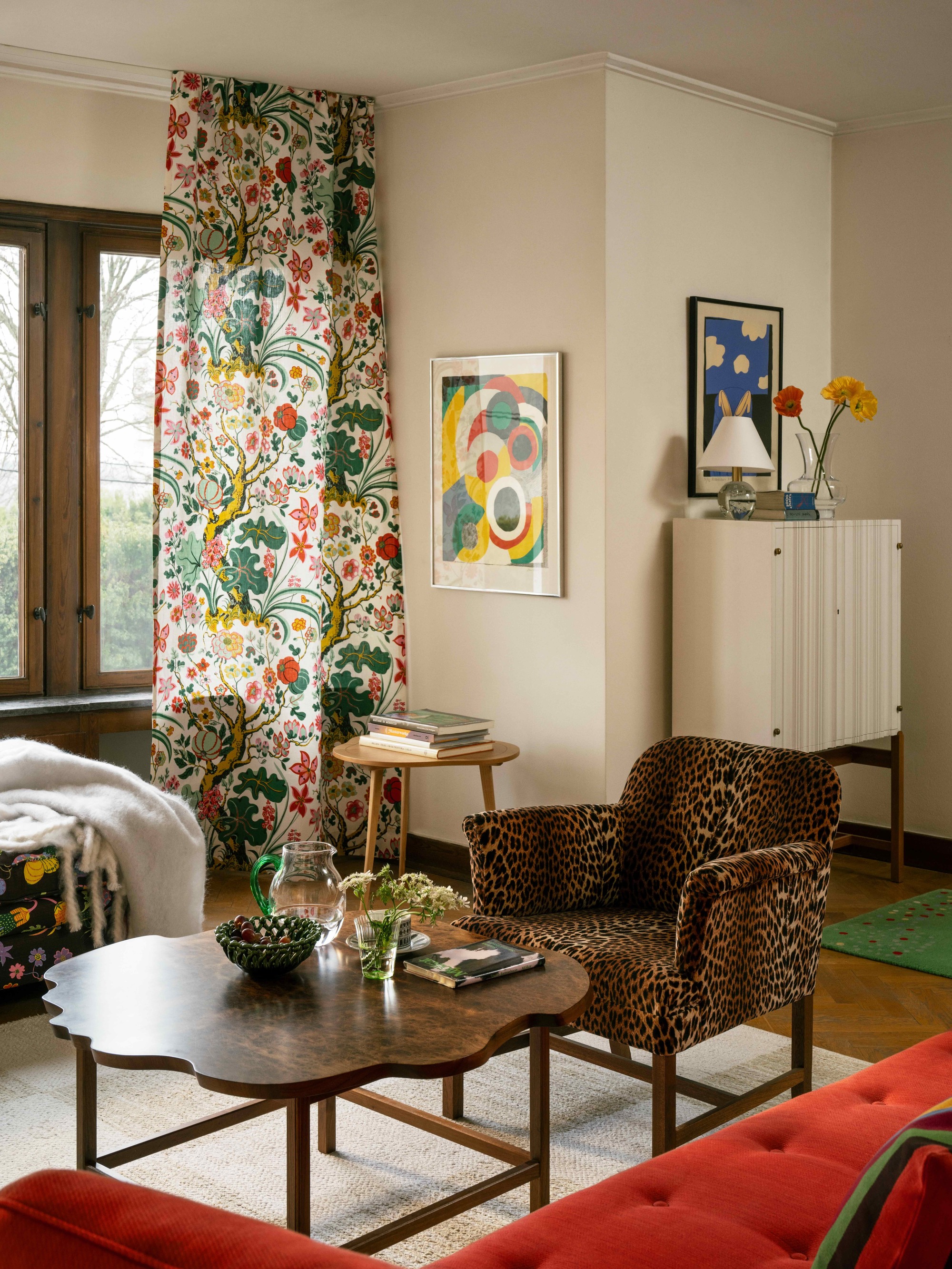 scandinavian maximalist living room with patterned curtain, leopard armchair, red sofa, timber coffee table, eclectic decor