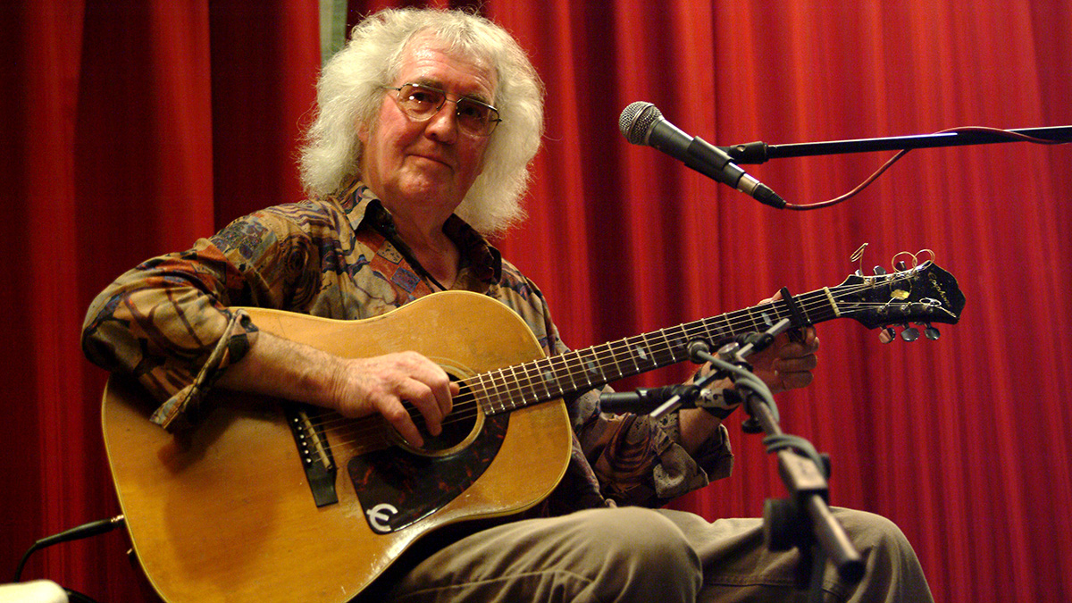 Wizz Jones playing acoustic guitar against a red background
