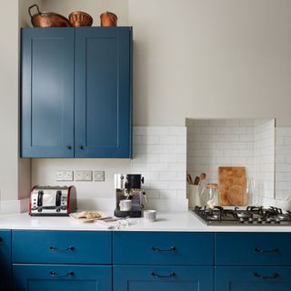 White painted kitchen with blue cabinets and a tiled backsplash, with kitchen appliances on the white worktop