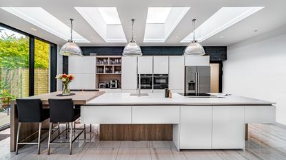White modern kitchen with skylights, pendant lighting and two level island
